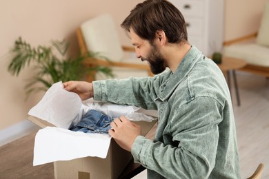 Photo of Happy man opening parcel at home. Internet shopping