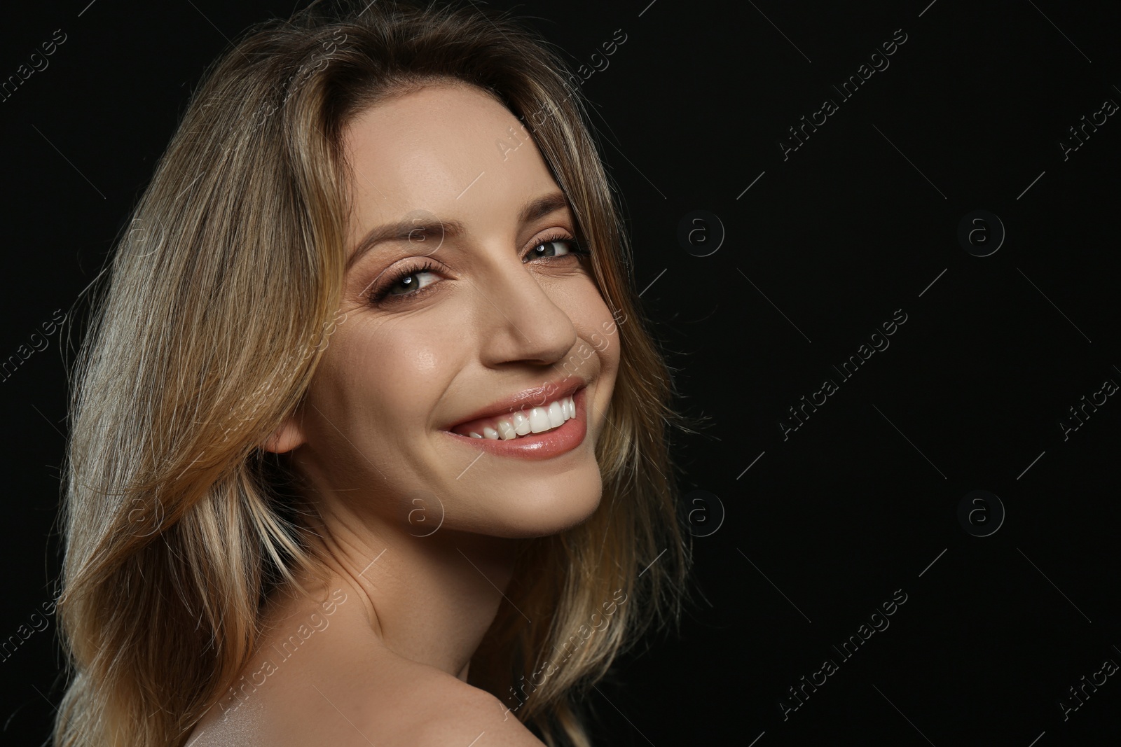 Photo of Portrait of happy young woman with beautiful blonde hair and charming smile on black background. Space for text