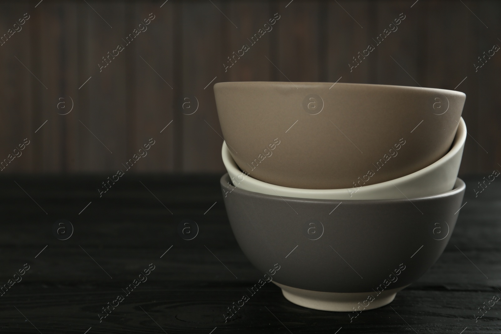Photo of Stylish empty ceramic bowls on black wooden table, space for text. Cooking utensils