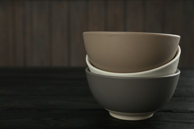 Photo of Stylish empty ceramic bowls on black wooden table, space for text. Cooking utensils
