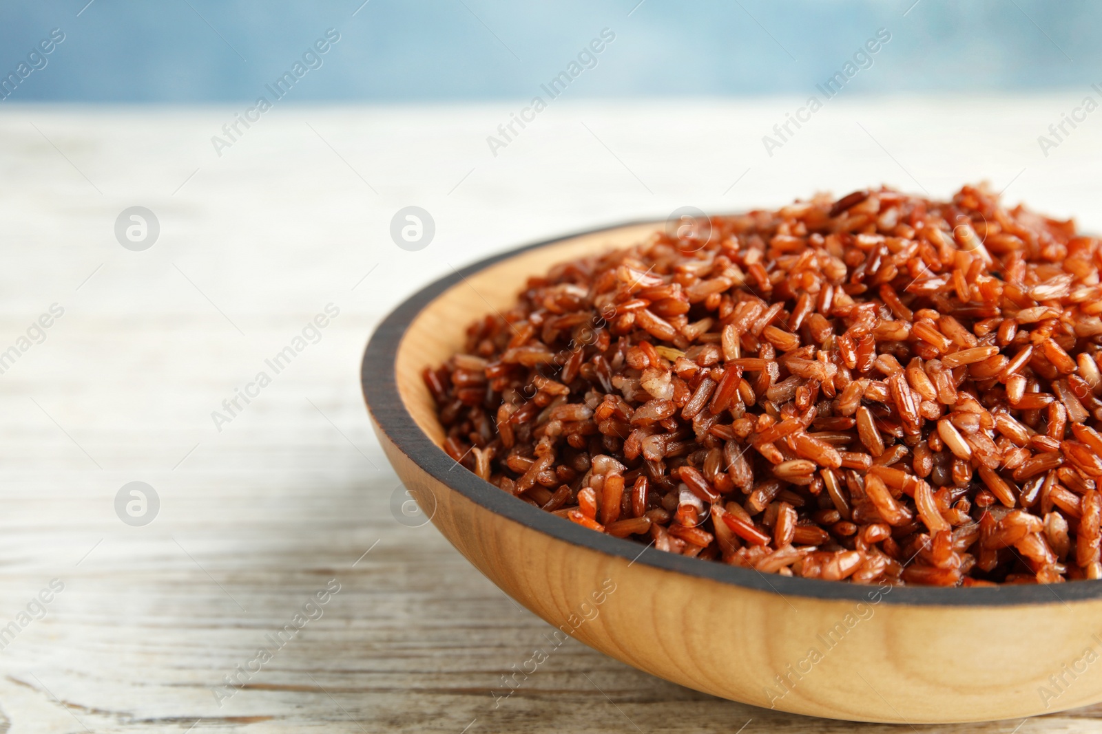 Photo of Bowl with delicious cooked brown rice on white wooden table, closeup. Space for text