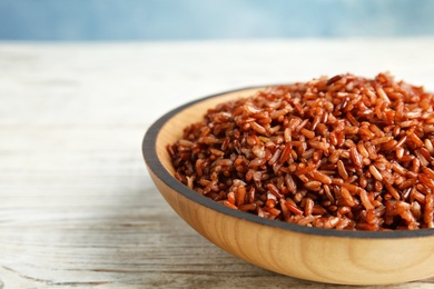 Photo of Bowl with delicious cooked brown rice on white wooden table, closeup. Space for text