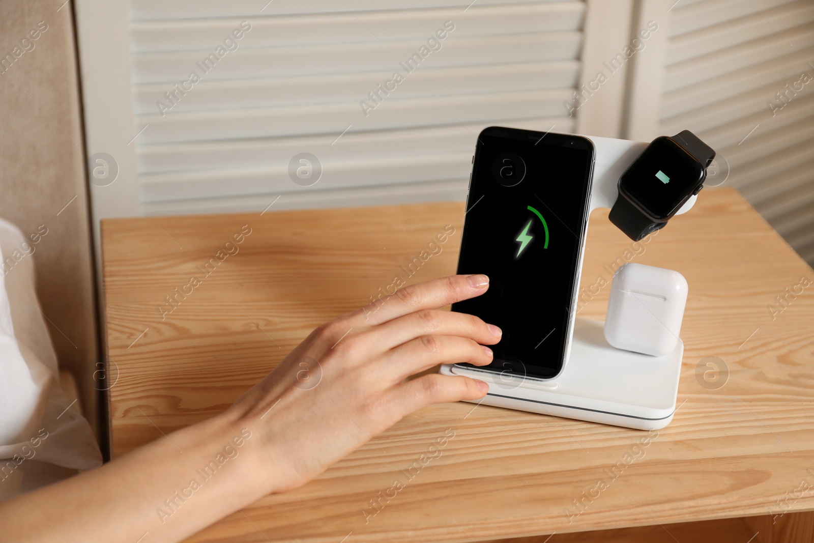 Photo of Woman taking smartphone from wireless charger in bedroom, closeup