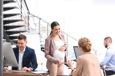 Photo of Young pregnant woman working with her employees in office