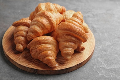 Photo of Wooden board with tasty croissants on grey table. French pastry