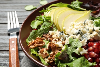 Photo of Tasty salad with pear slices and fork on black wooden table, closeup