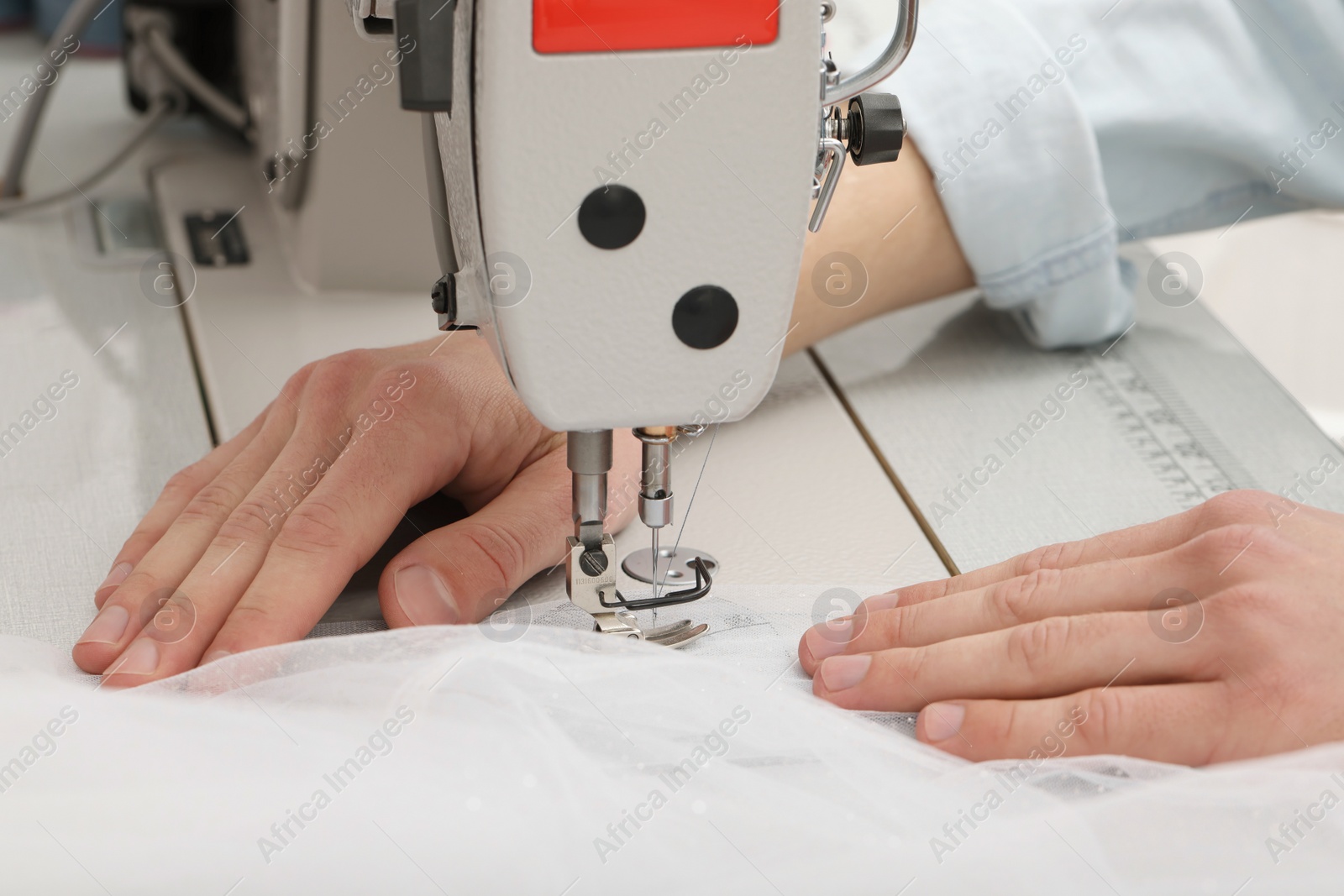 Photo of Dressmaker sewing new dress with machine in atelier, closeup