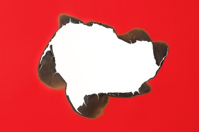 Photo of Burnt hole in red paper on white background, space for text
