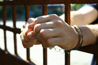 Photo of Man handcuffed in jail outdoors, closeup. Criminal law