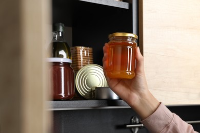 Photo of Woman with jar of honey near shelf indoors, closeup. Food donation