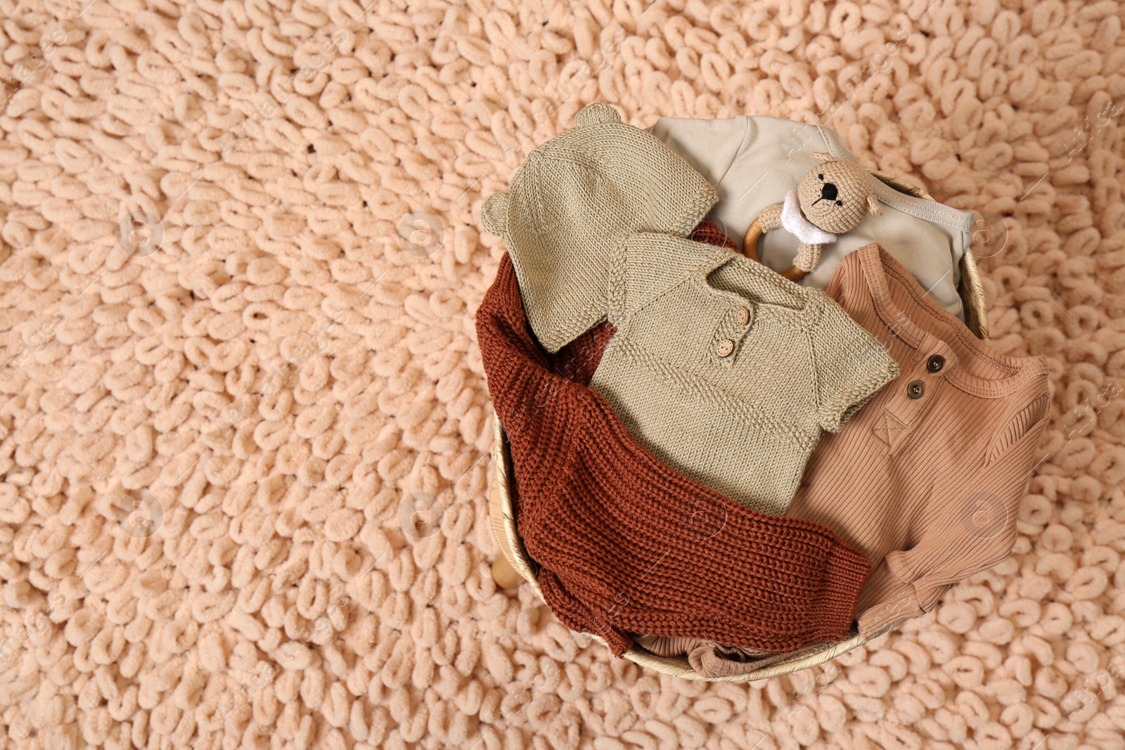Photo of Laundry basket with baby clothes, shoes and crochet toy on beige rug, top view. Space for text
