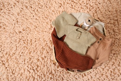 Laundry basket with baby clothes, shoes and crochet toy on beige rug, top view. Space for text
