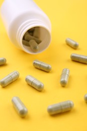 Photo of Jar with vitamin capsules on yellow background, closeup