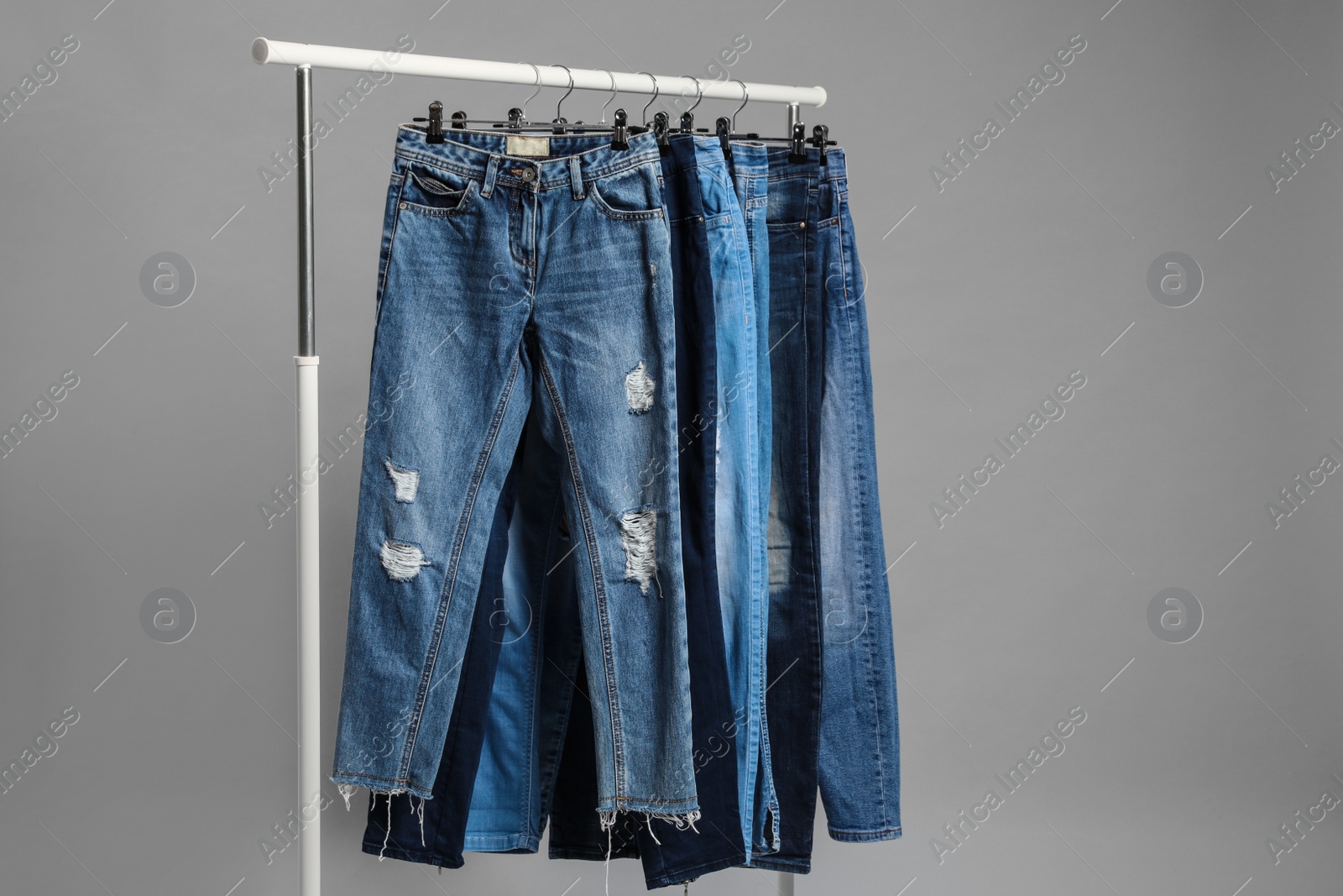 Photo of Rack with different jeans on grey background