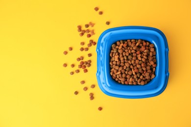 Dry pet food in feeding bowl on yellow background, flat lay. Space for text