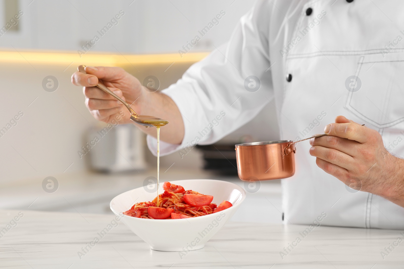 Photo of Professional chef pouring sauce into delicious spaghetti at marble table, closeup
