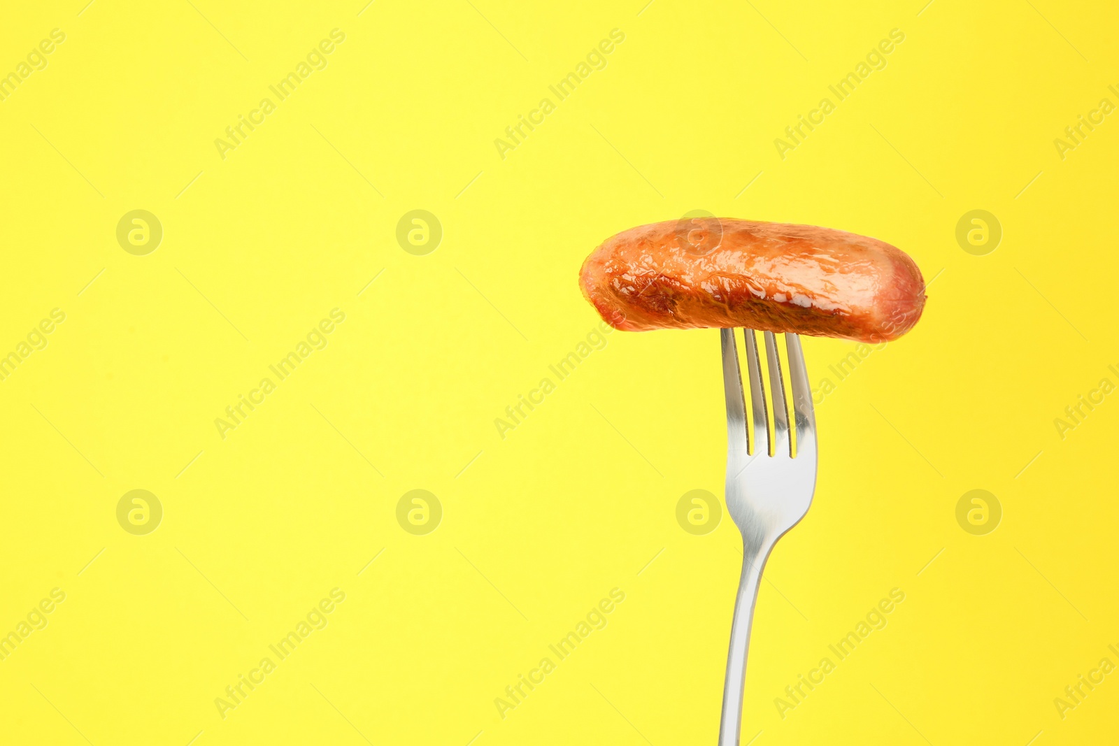 Photo of Fork with tasty fried sausage on yellow background. Space for text