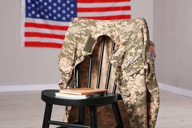 Photo of Chair with soldier uniform and notebooks near flag of United States indoors. Military education
