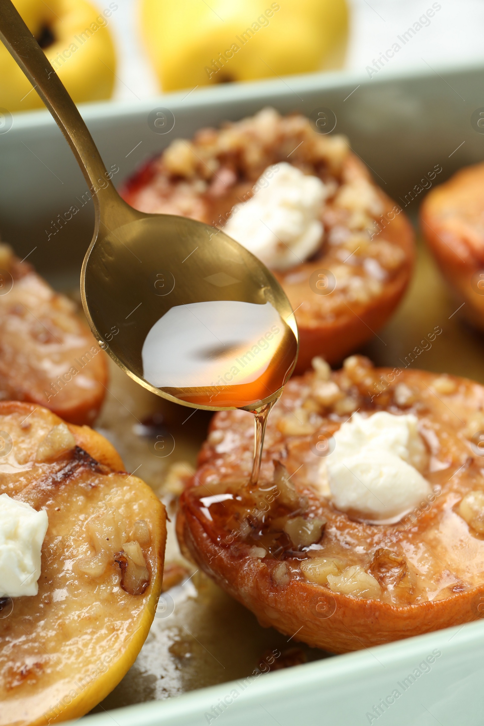 Photo of Pouring honey onto tasty baked quinces with nuts and cream cheese in dish, closeup