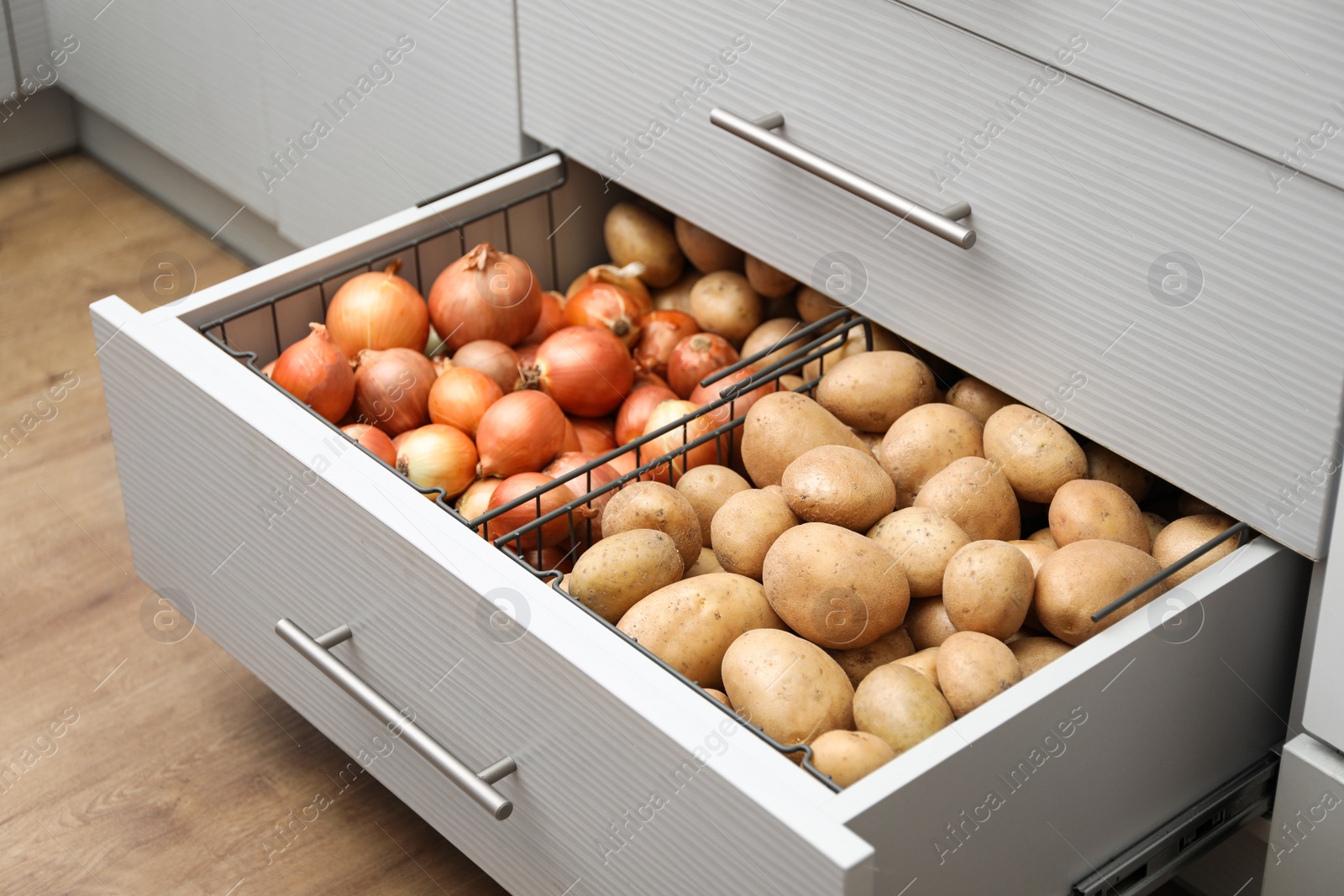 Photo of Open drawer with potatoes and onions in kitchen. Orderly storage