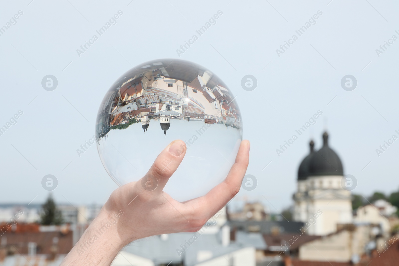 Photo of View of beautiful city street, overturned reflection. Man holding crystal ball against sky, closeup