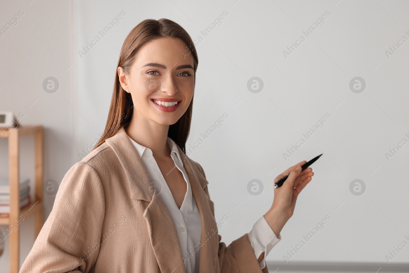Photo of Happy young teacher explaining something at whiteboard in classroom