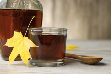 Photo of Tasty maple syrup, spoon and leaf on wooden table, closeup. Space for text