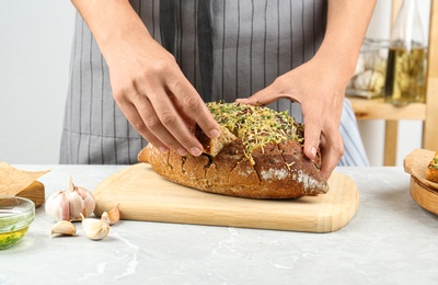 Photo of Woman taking piece of tasty homemade garlic bread with cheese and herbs at grey table, closeup