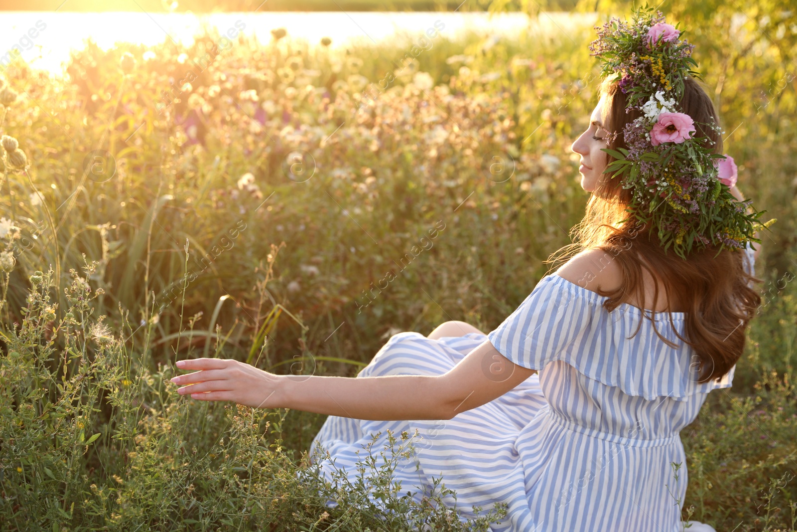 Photo of Young woman wearing wreath made of beautiful flowers outdoors on sunny day