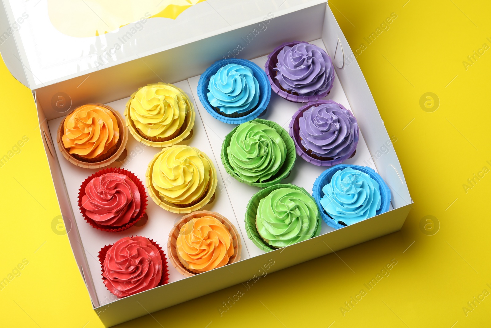 Photo of Tasty cupcakes in box on yellow background, above view