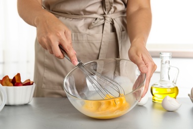 Photo of Woman whipping eggs at grey table, closeup. Cooking of delicious cake
