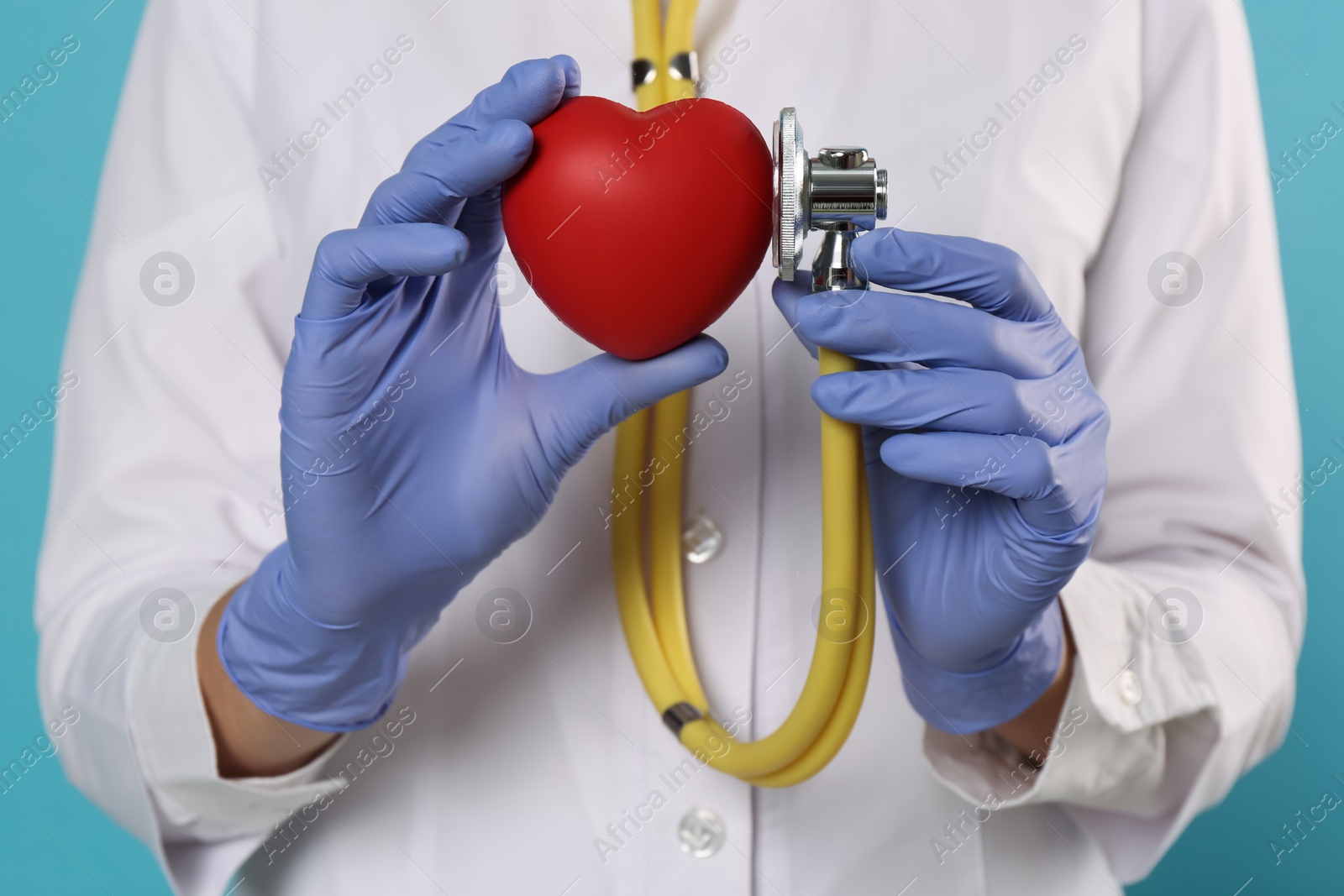 Photo of Doctor with stethoscope and red heart on light blue background, closeup. Cardiology concept