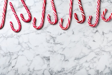 Photo of Sweet Christmas candy canes on white marble background, flat lay. Space for text