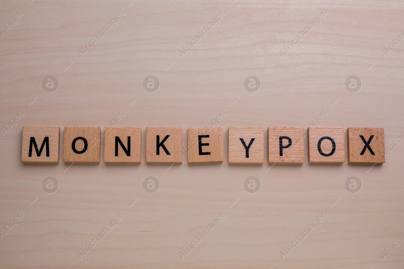 Photo of Word Monkeypox made of squares on wooden table, top view