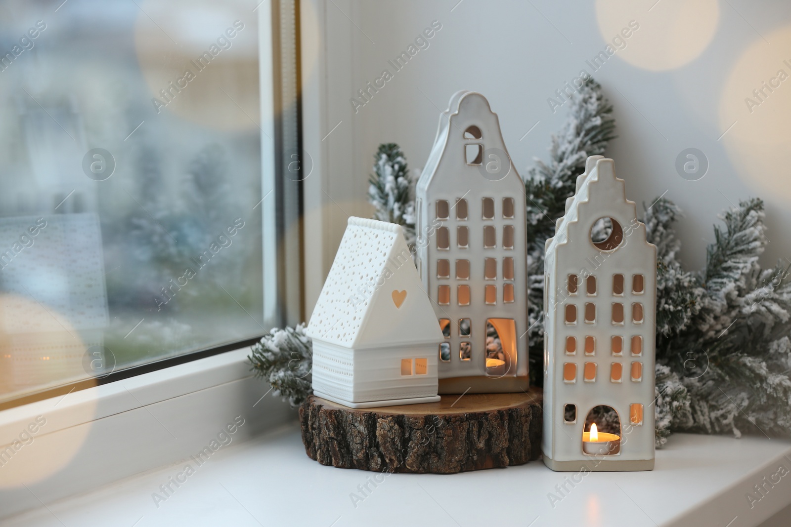 Photo of Beautiful house shaped candle holders and Christmas decor on windowsill indoors, space for text. Bokeh effect