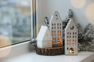 Photo of Beautiful house shaped candle holders and Christmas decor on windowsill indoors, space for text. Bokeh effect