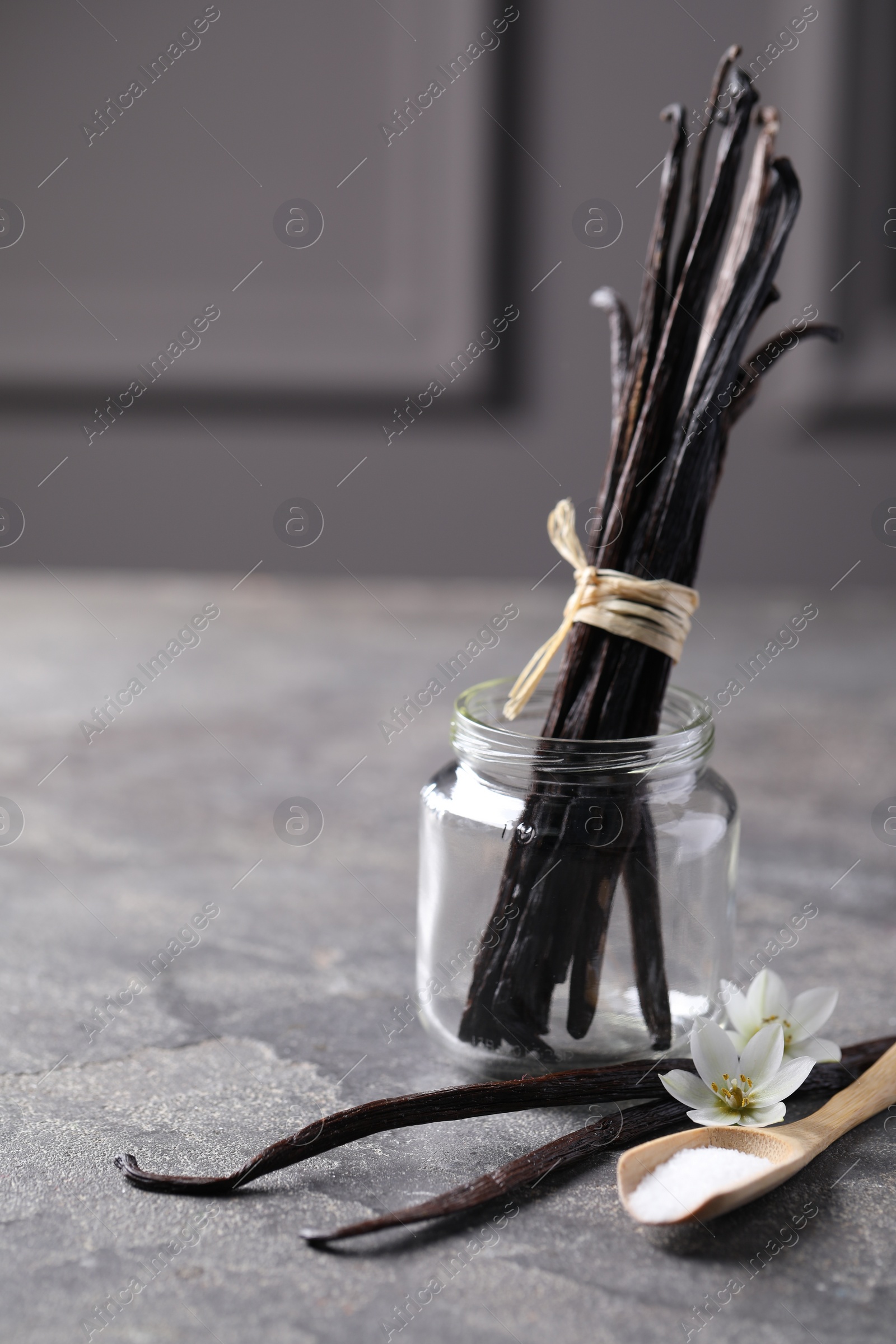 Photo of Spoon with sugar, flowers and vanilla pods on grey textured table. Space for text