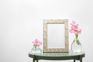 Photo of Blank frame and vases with flowers on table against white background. Mock up for design