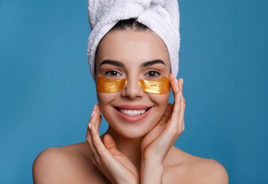 Photo of Beautiful young woman with under eye patches and hair wrapped in towel on light blue background