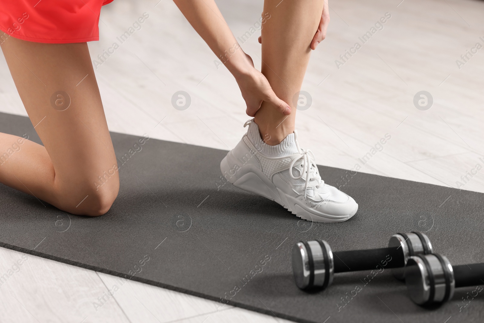 Photo of Woman suffering from leg pain on exercise mat indoors, closeup