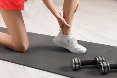 Photo of Woman suffering from leg pain on exercise mat indoors, closeup
