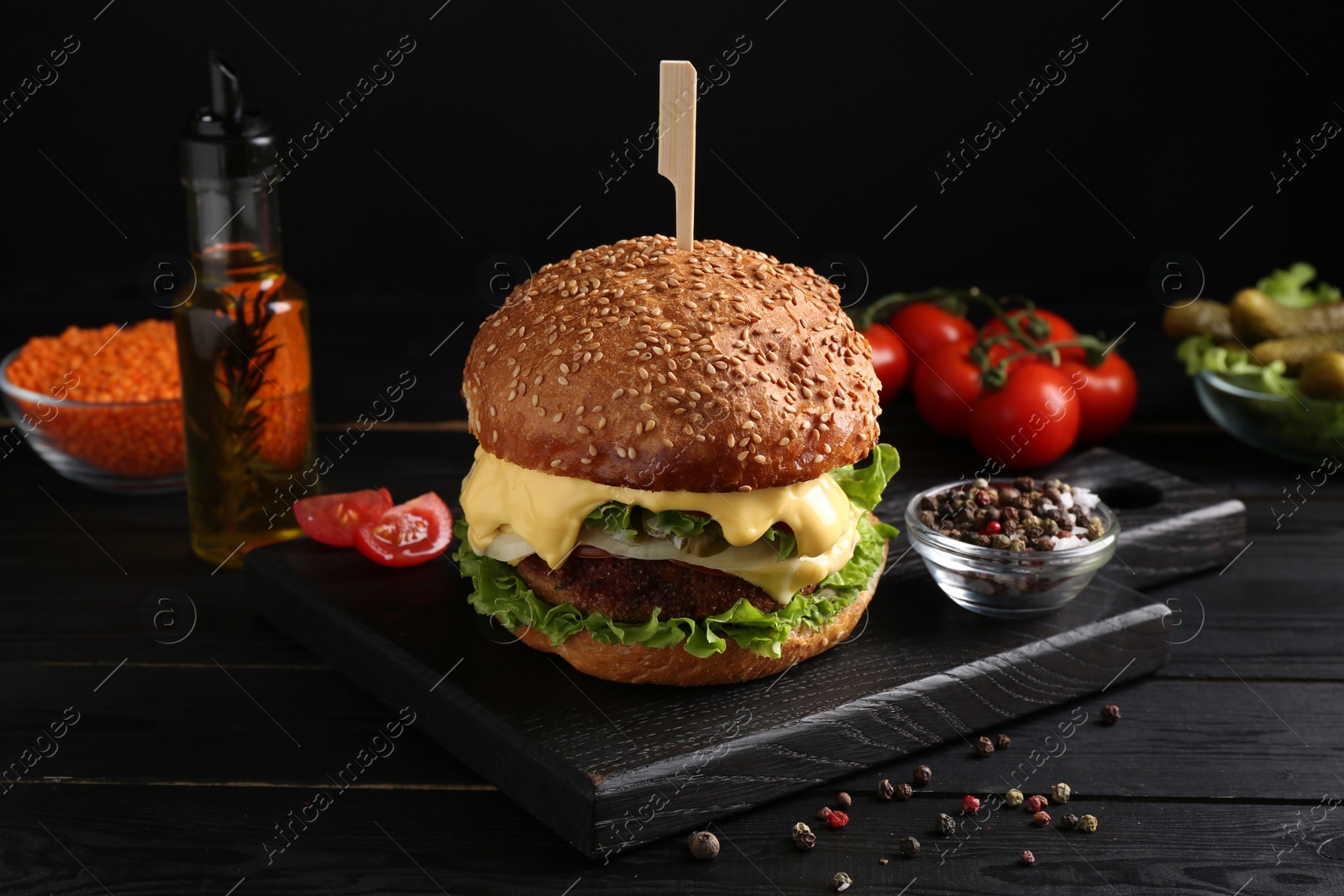 Photo of Tasty vegetarian burger and ingredients on black wooden table