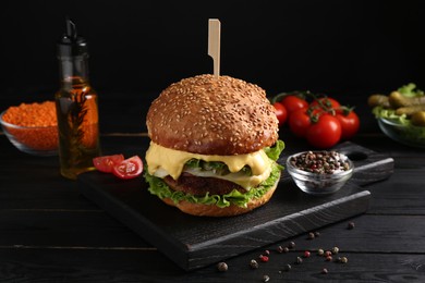 Tasty vegetarian burger and ingredients on black wooden table