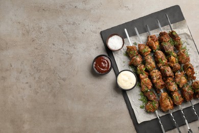 Metal skewers with delicious meat and sauces served on light grey table, flat lay. Space for text