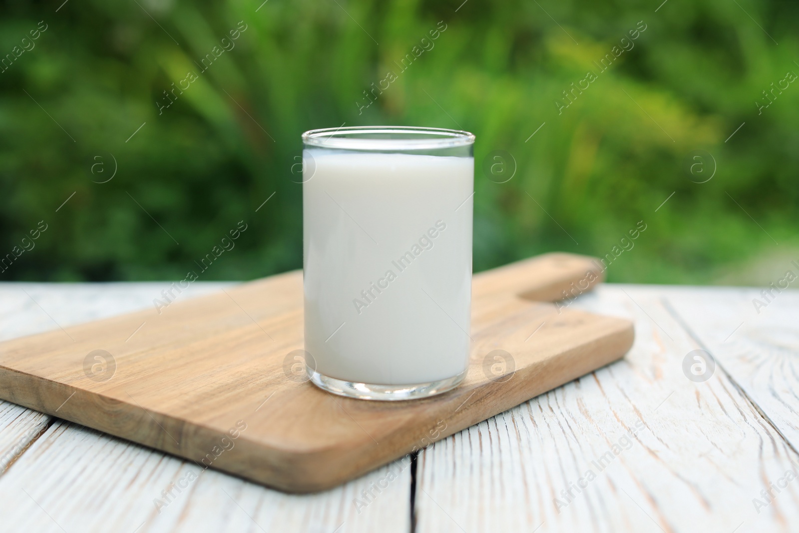 Photo of Glass of tasty fresh milk on white wooden table outdoors