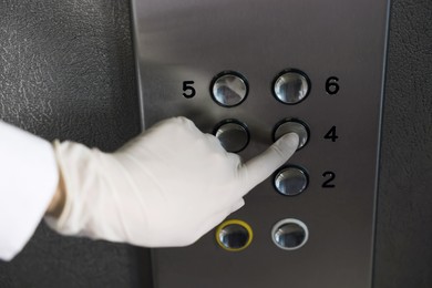 Woman wearing medical glove choosing floor in elevator, closeup. Protective measure