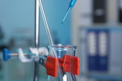 Photo of Laboratory analysis. Dripping blue liquid into flask on stand indoors, closeup