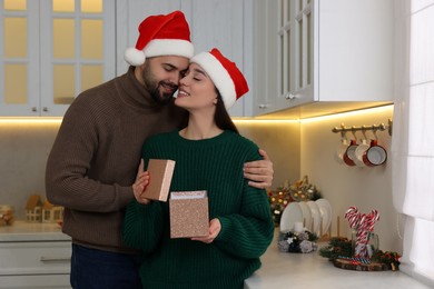 Beautiful young woman in Santa hat opening Christmas gift from her boyfriend at home