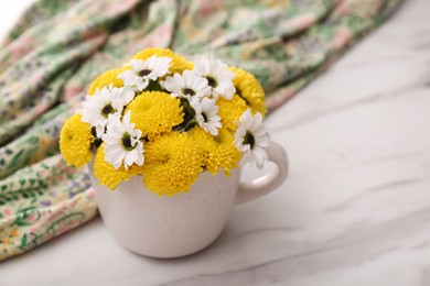 Beautiful bright flowers in cup and fabric on white marble table, closeup