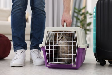 Photo of Travel with pet. Man near carrier with cute cat at home, closeup